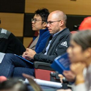 A diverse group of adults attentively listening to a lecture in an indoor conference setting.