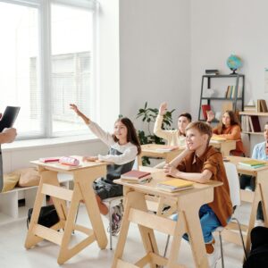 Students engage eagerly in a classroom, raising hands and participating in a lesson with their teacher.